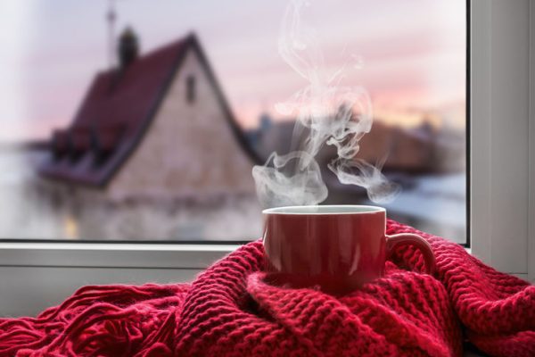 cup with a hot drink on the windowsill in the background of a winter city. Focus on the edge of the cup