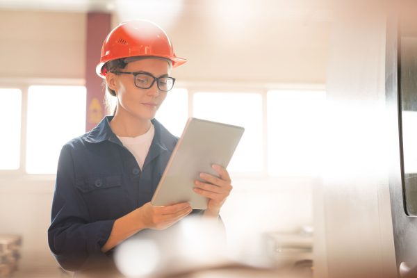 Young confident female technician looking through online data in tablet while checking technical points